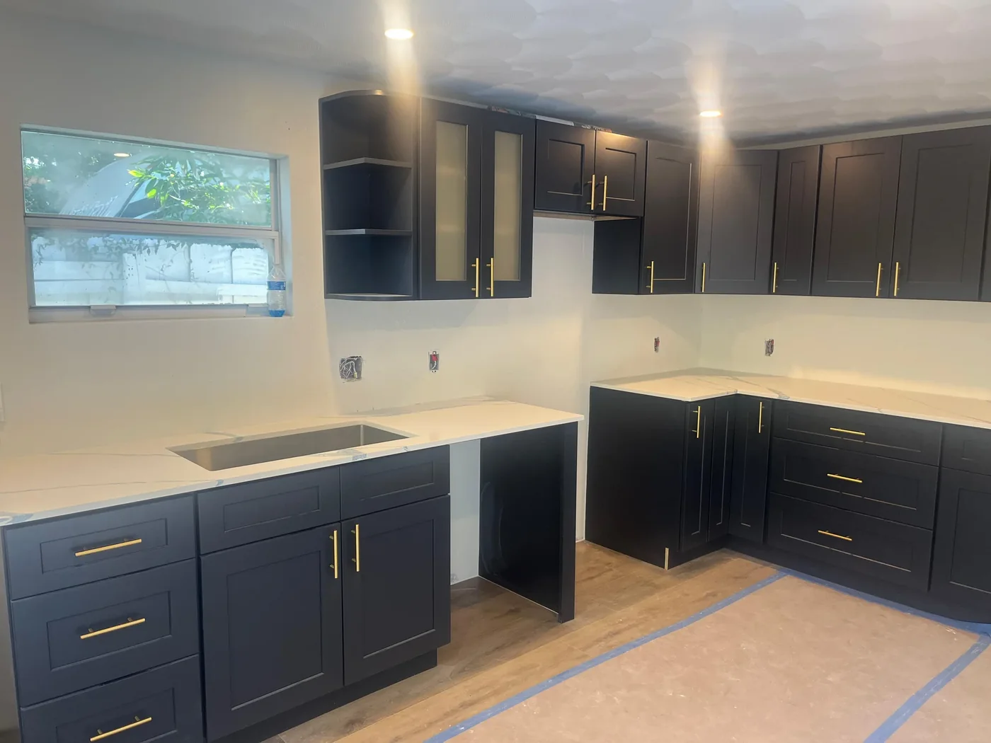 Navy shaker kitchen mid-install: cabinets set, stone countertops in place and the floor covered with protection paper